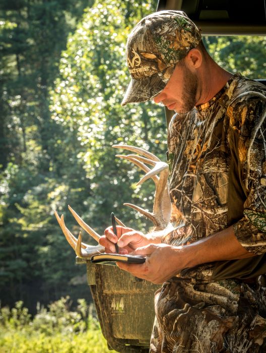 Hunter writing in notebook with 400H-190 with antlers in background
